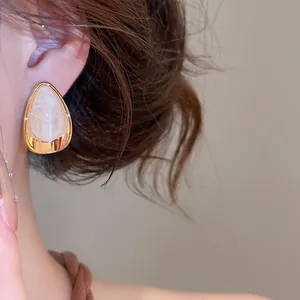 Détail d'une boucle d'oreille goutte en acrylique avec bordure dorée portée sur l'oreille