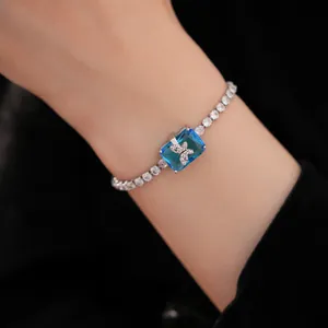 Dettaglio di un bracciale argentato con pietra blu quadrata e farfalla di zirconi.