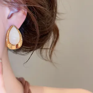 Gros plan détaillé de boucles d'oreilles goutte en acrylique crème avec cadre doré poli