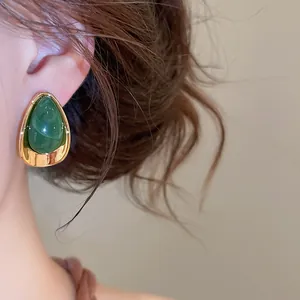Gros plan d'une boucle d'oreille en acrylique vert en forme de goutte et base dorée