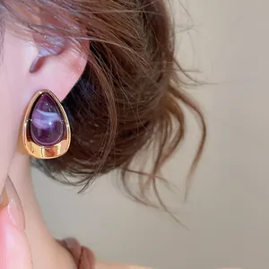 Gros plan d'une élégante boucle d'oreille goutte en acrylique violet avec bordure dorée
