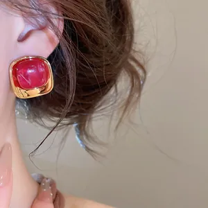 Gros plan d'une boucle d'oreille carrée dorée avec pierre acrylique rouge sur le modèle.