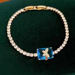 Vista dettagliata di un bracciale tennis placcato oro con zircone blu e ciondolo a farfalla.