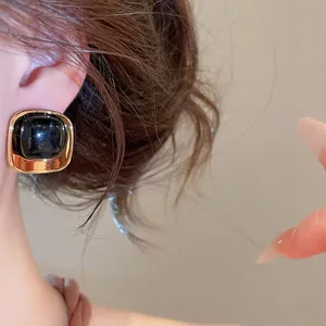 Vue détaillée de boucles d'oreilles carrées en acrylique doré et noir sur l'oreille.