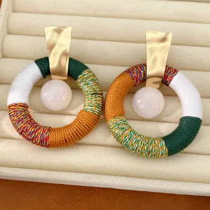 Detail van handgemaakte kleurrijke katoenen touw oorbellen met een witte harskraal in het midden.