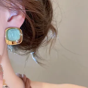 Gros plan d'une élégante boucle d'oreille carrée dorée avec centre acrylique vert menthe