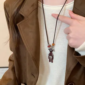 Detailansicht einer braunen Bärenkette, getragen über einem weißen Pullover und Sakko