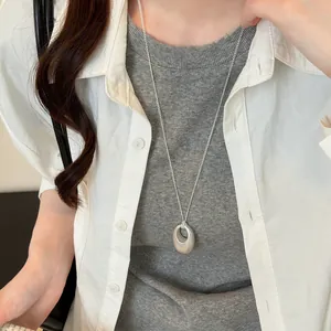 Detailaufnahme einer ovalen, matt-silbernen Anhänger-Halskette zu einem Freizeitoutfit.