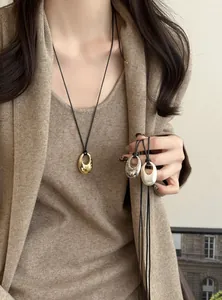 Nahaufnahme von minimalistischen ovalen Anhänger-Halsketten in Gold und Silber an Kordeln.