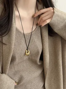 Detailansicht eines goldenen ovalen Anhängers an einer schwarzen Lederkordelkette