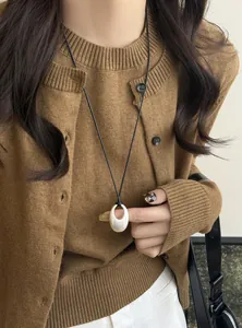 Detailansicht einer ovalen Anhängerkette im koreanischen Stil auf einem braunen Strickpullover.
