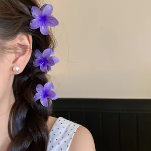 Gros plan de trois pinces à cheveux en acrylique violette en forme de fleur dans une tresse.