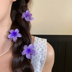 Détail de trois mini pinces à cheveux fleurs en acrylique violet sur une tresse foncée.