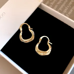 Detailopname van gouden U-vormige creolen met geplooide textuur in een zwart juwelendoosje