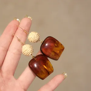 Detailed close-up view of raffia and marbled brown acrylic square pendant hook earrings