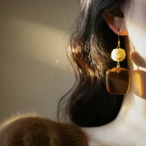 Close-up of French vintage raffia and brown acrylic square pendant hook earring on model