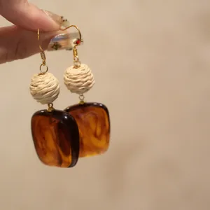 Hand-held detail of vintage-style raffia ball and amber acrylic square drop earrings