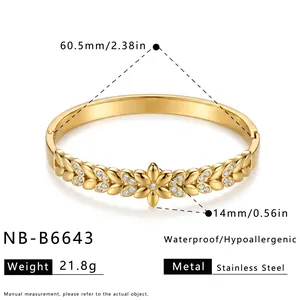 Close-up detail of flower patterned stainless steel bangle with gold finish and rhinestones.