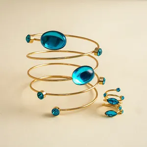 Detail eines zweiteiligen goldfarbenen Spiralarmbands und Rings mit blauen Steinen.