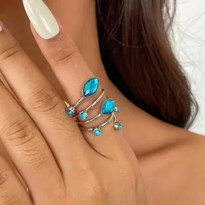 Detailansicht eines silbernen Wickelrings mit funkelnden blauen Acrylsteinen an einer Hand