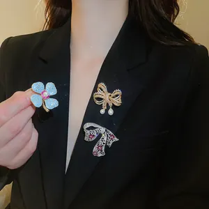 Detailopname van sprankelende zirkoonbloem- en strikbroches met parels op een zwarte blazer.