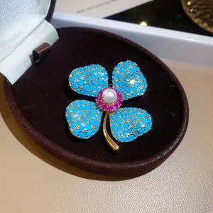 Detailopname van een bloemenbroche met turquoise stenen en een witte centrale parel