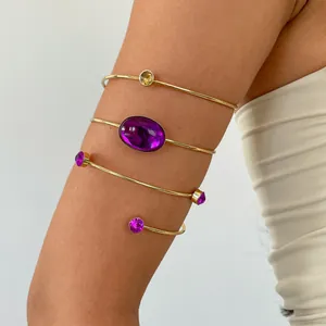 Detailansicht von goldenen Vintage-Armreifen mit lila Acrylsteinen am Arm eines Modells