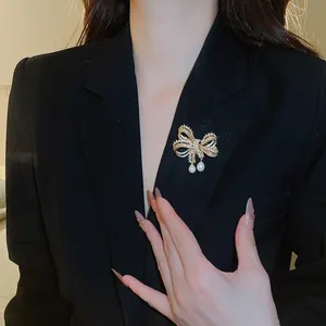 Elegante strik-broche met sprankelende zirkonia en hangende parels op zwarte blazer.