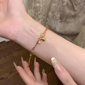 Dettaglio di bracciale placcato oro con cordino rosso, zircone e ciondolo a campana