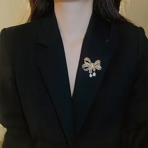 Elegante goudkleurige strikbroche met zirkonia pavé en parelhangers op een zwarte blazer