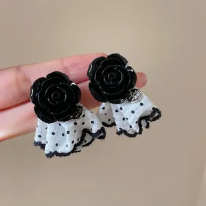 Macro view of black rose stud earrings featuring white polka dot skirt fabric and lace.