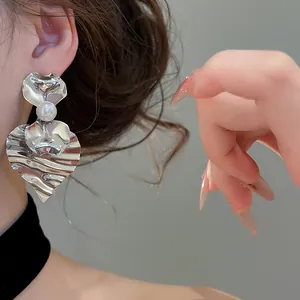 Elegante zilveren geplooide hart oorbellen met parel detail op een model getoond.