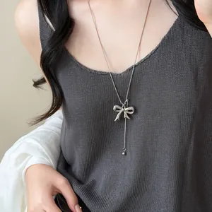 Detailed view of an elegant silver bowknot Y-necklace on a model wearing grey knitwear