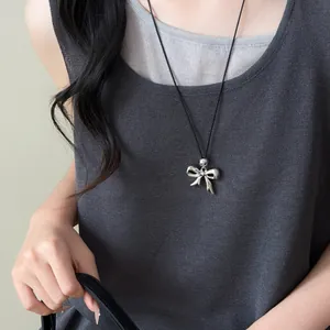Detail view of a silver bow pendant necklace on a black cord worn with a grey knit top.
