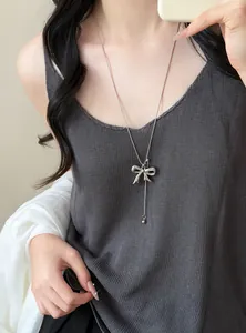 Elegant silver bow pendant necklace on a long chain worn over a gray sweater detail view