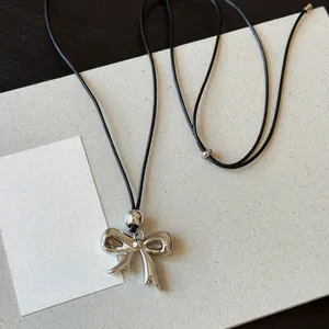 Macro view of a silver metallic bow pendant on an adjustable black cord necklace.