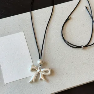 Detail of matte silver bow pendant on adjustable black leather cord necklace.