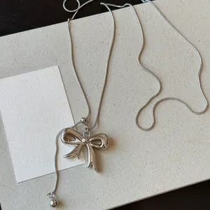 Close-up of a silver bow pendant on a delicate snake chain with adjustable slider.