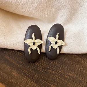 Close-up of vintage elliptical wooden stud earrings with a beige orchid flower design