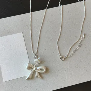 Detail view of matte bow pendant necklace with clear and white beads on grey paper.
