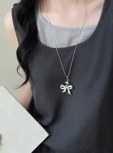 Detail shot of a minimalist silver bow pendant long sweater chain necklace on a model