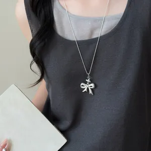 Detailed macro view of a minimalist matte silver bow pendant necklace worn by a model.