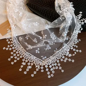 Close-up of white lace mesh scarf with delicate floral embroidery and tassel trim