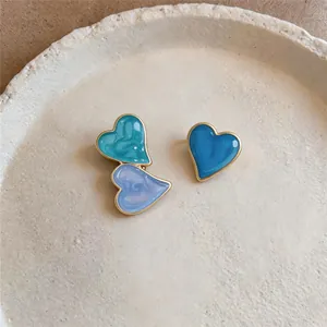 Close-up of asymmetric blue heart stud earrings with dripping oil finish and golden edges