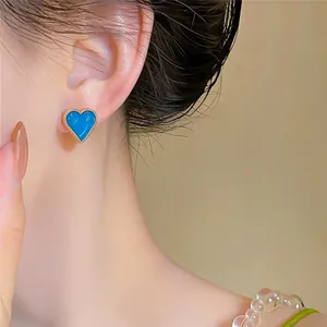 Macro view of a vibrant blue heart-shaped oil-drop stud earring worn on a female ear