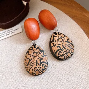 Macro detail of retro wooden teardrop earrings featuring intricate black floral patterns