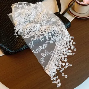 Detailed view of white lace mesh scarf with intricate floral embroidery and fringe.