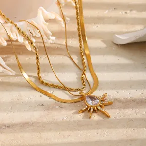 Detailweergave van goudvergulde drielaagse ketting met zonnestraal kristallen hanger.