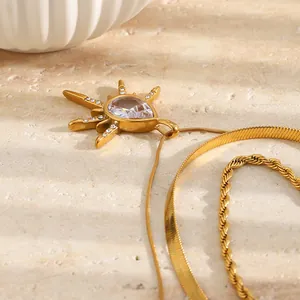 Detailopname van een drielaagse 18K vergulde ketting met kristallen zonnestraal hanger