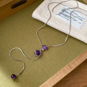 Détail d'un collier chaîne serpent argentée avec perles violettes et pendentif hexagramme.